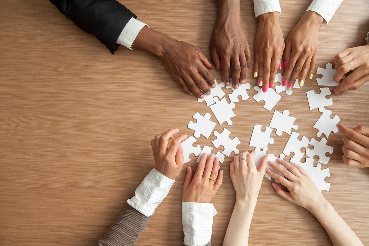 hands-of-multi-ethnic-business-team-assembling-jigsaw-puzzle-top-view
